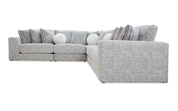 Large L-shaped sectional sofa in light gray fabric with multiple textured and round white accent pillows, modern design for spacious living rooms.