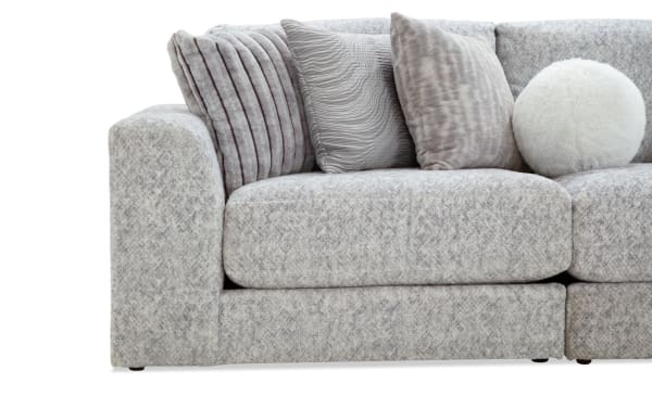 Gray fabric sectional sofa with plush cushions and a variety of textured throw pillows, including a round white furry pillow, showcasing modern living room comfort.