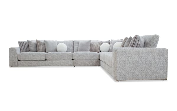 Large L-shaped sectional sofa upholstered in light gray textured fabric with multiple decorative throw pillows in various shades of gray and white, ideal for modern living room seating.