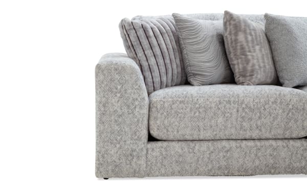 Modern gray fabric sofa with thick cushions and multiple textured throw pillows in various shades of gray, showcasing a cozy and stylish living room seating option.