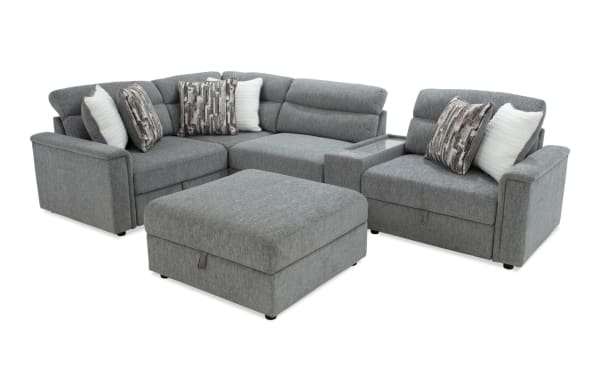 Gray fabric sectional sofa set with cushioned seats, backrests, and matching ottoman, featuring patterned and solid throw pillows.