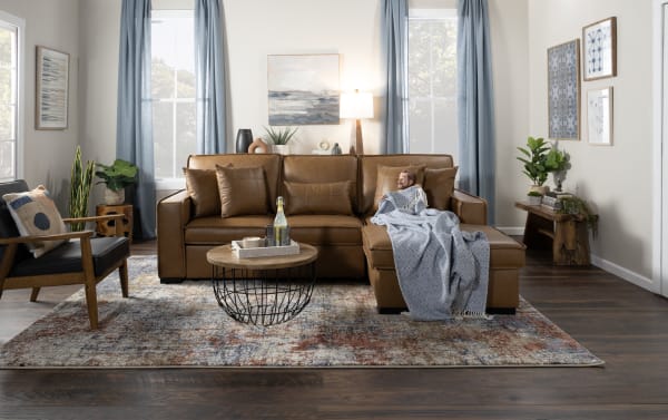 Brown leather sectional sofa with multiple cushions, a wooden coffee table, gray throw blanket, indoor plants, and modern living room decor.