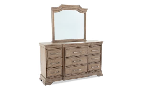 Wooden dresser with a large decorative mirror, featuring nine drawers with metal handles, in a light brown finish and classic design.