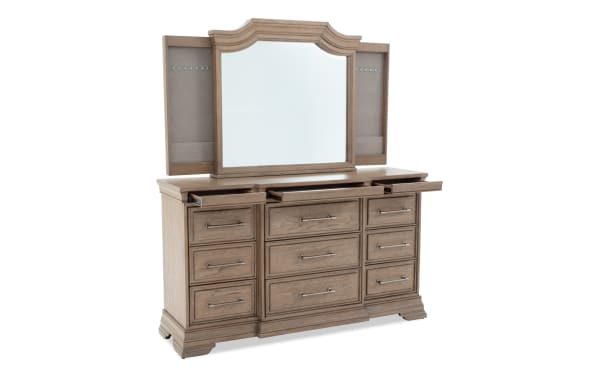 Wooden dresser with a large framed mirror, nine drawers with metal handles, and three top pull-out trays, in a light brown finish.