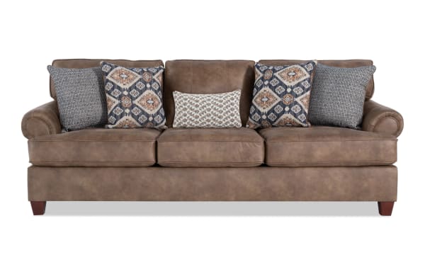 Traditional Raleigh collection sofa in cognac brown faux leather upholstery with plush cushions, patterned accent pillows, and polyester fabric material.