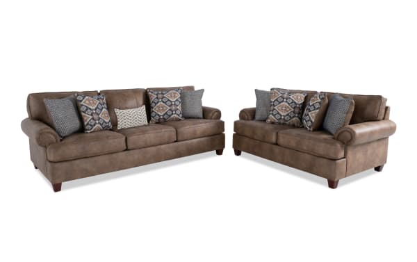 Two brown leather sofas with rolled arms and wooden legs, each featuring multiple decorative patterned and textured throw pillows, ideal for living room seating.