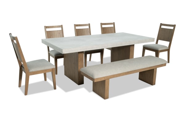 Monterey 7 Piece Natural & Gray Panel Back Upholstered Dining Set with Bench featuring a faux concrete melamine top, gray polyester fabric seats, and traditional rubberwood solid frames.