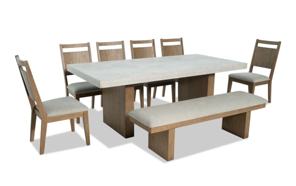 Monterey 8 Piece Natural & Gray Panel Back Upholstered Dining Set with Bench featuring a faux concrete melamine tabletop, six gray fabric Bob-O-Pedic® Memory Foam chairs, and a matching upholstered bench in traditional style. Made with MDF, rubberwood, Asian hardwood, pine veneer, and polyester fabric.