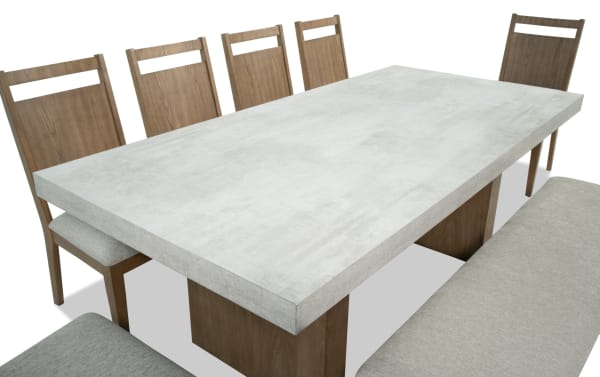 Monterey 8 Piece Natural & Gray Panel Back Upholstered Dining Set with bench, featuring gray polyester fabric chairs, faux concrete melamine table top, and traditional rubberwood frame.