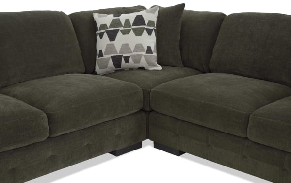 Dark green sectional sofa with plush cushions and two decorative pillows, one with a geometric pattern in neutral tones, showcasing modern fabric upholstery.