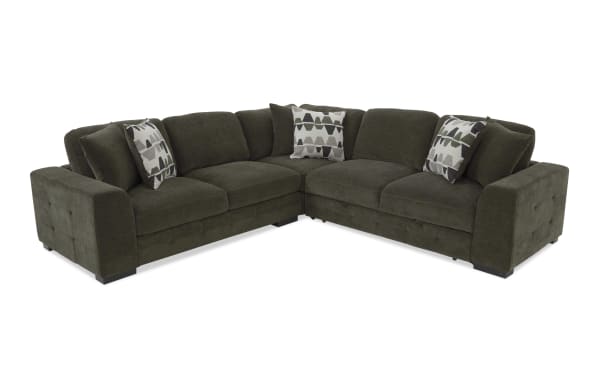Dark green fabric sectional sofa with tufted armrests, thick cushions, and three patterned throw pillows, designed for modern living rooms.