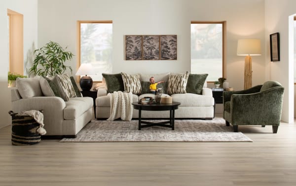 Modern living room with beige fabric sofas, green velvet armchair, black round coffee table, decorative pillows, knit throw, and natural wood floor lamp.