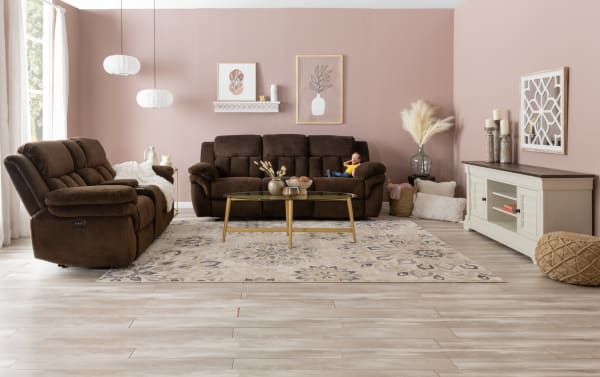 Living room with brown corduroy reclining sofas, glass coffee table with gold legs, beige floral rug, pink walls, and modern decor.