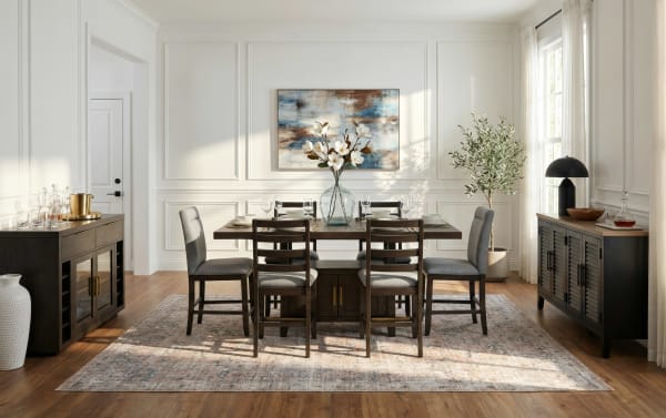 Modern dining room with dark wood table and six gray upholstered chairs on patterned area rug, featuring floral centerpiece and abstract wall art.