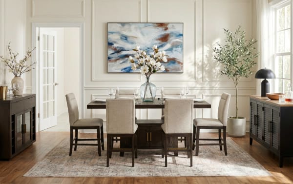 Modern dining room with a dark wood rectangular table, six beige upholstered chairs, floral centerpiece in glass vase, abstract wall art, and natural light.