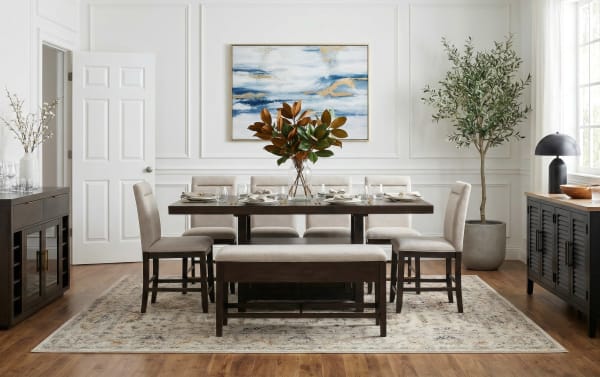 Modern dining room with dark wood table, beige upholstered chairs and bench, decorative centerpiece, abstract wall art, and large potted plant.