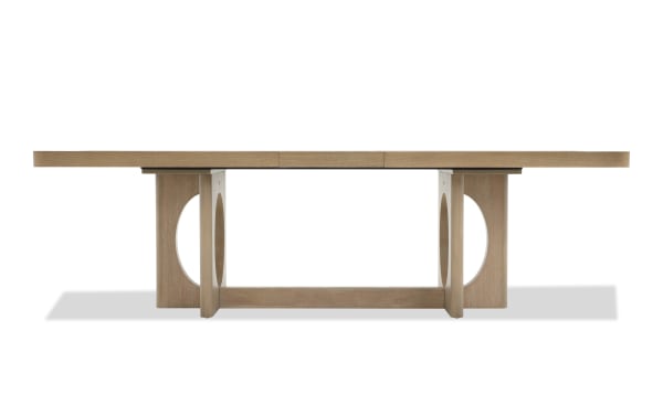 Rectangular wooden dining table with a light oak finish, featuring a modern design with circular cutouts on the sturdy legs and a smooth, flat tabletop.