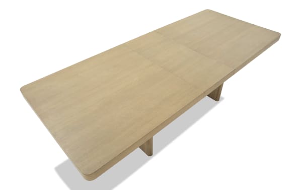 Light wood rectangular dining table with rounded edges and a smooth finish, featuring a central extension leaf and sturdy wooden legs.