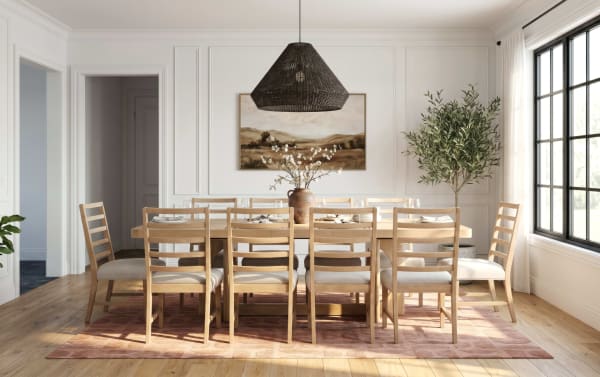 Dining room with a large light wood table and ten matching ladder-back chairs with beige cushions, a woven black pendant light, a landscape painting, and natural light from a large window.
