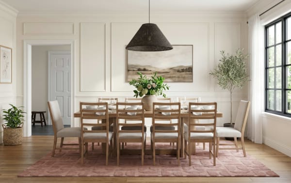 Modern dining room with a wooden table and eight cushioned chairs on a textured pink rug, featuring a large window, green plants, and neutral decor.
