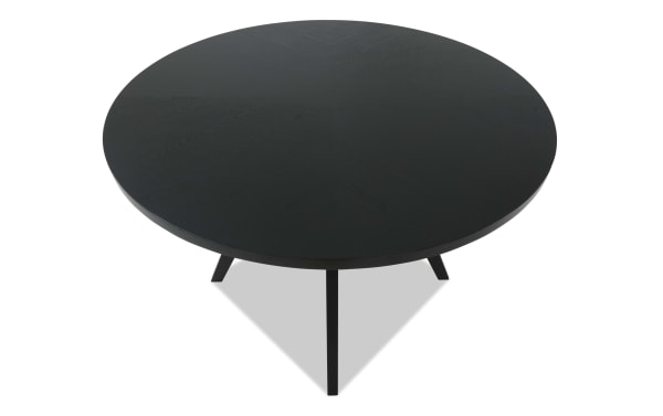 Round black wooden dining table with three angled legs, featuring a smooth matte finish and modern minimalist design.