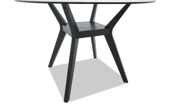 Round dining table with black wooden legs and a glass top, featuring a modern geometric base design for contemporary interiors.
