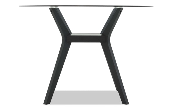 Modern round glass-top table with black wooden angled legs and a small rectangular shelf, ideal for contemporary dining or office spaces.