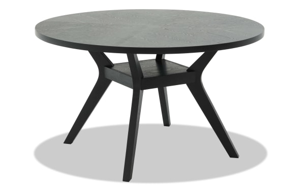 Round black wooden dining table with angled legs and a small central shelf, modern minimalist design for home or office.