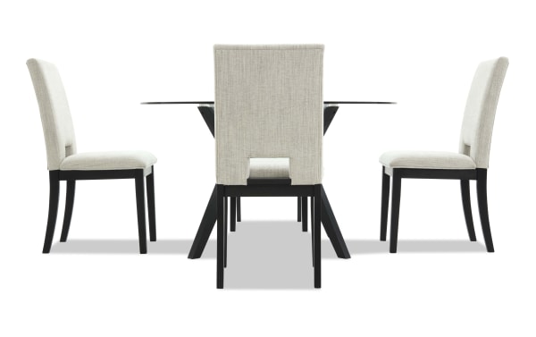 Modern dining set with four beige upholstered chairs featuring black wooden legs and a glass-top table with black angled legs, ideal for contemporary interiors.