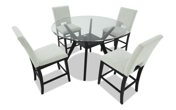 Round glass dining table with black wooden legs and four light gray upholstered chairs, modern kitchen furniture set.