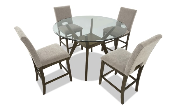 Round glass-top dining table with dark wood base and four beige upholstered chairs, featuring cushioned seats and high backs.