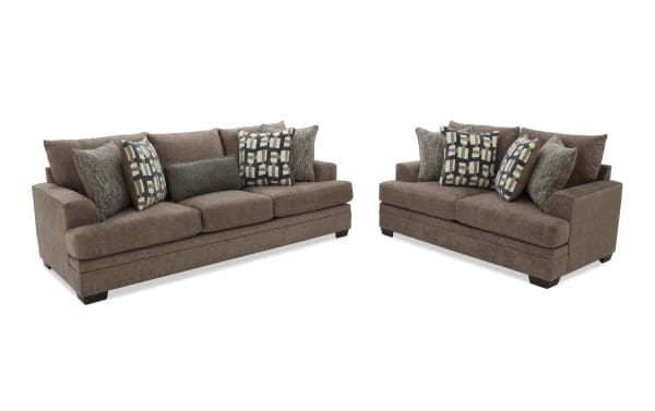 Two brown fabric sofas with plush cushions and patterned throw pillows, featuring a modern design with wide armrests and dark wooden legs, ideal for living room seating.