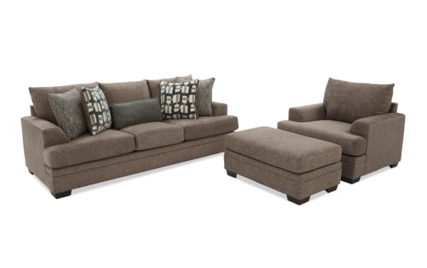 Brown fabric living room set with three-seat sofa, armchair, and matching ottoman, featuring patterned throw pillows and dark wooden legs.