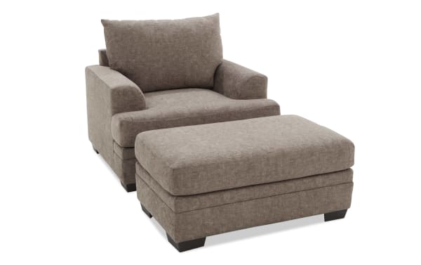 Brown fabric armchair with matching ottoman, featuring plush cushions, wide armrests, and dark wooden legs, ideal for living room seating.