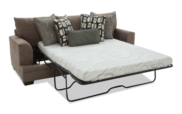 Brown fabric sofa bed with a white patterned mattress and five decorative pillows, featuring a metal fold-out frame for guest sleeping.