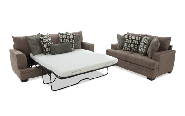 Brown fabric sectional sofa with multiple patterned throw pillows, featuring a pull-out metal frame bed with white mattress for space-saving functionality.