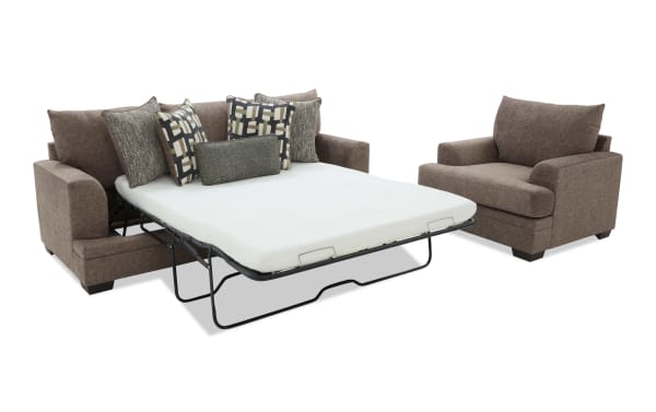 Brown fabric sleeper sofa with geometric patterned throw pillows and a matching armchair, featuring a pull-out metal frame bed with white mattress.