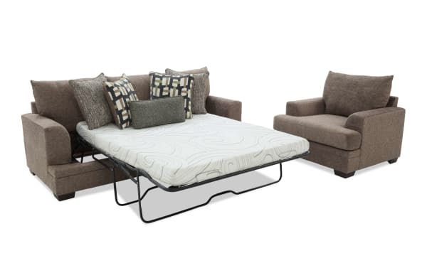 Brown fabric sleeper sofa with a white patterned mattress pulled out, featuring multiple decorative pillows, paired with a matching brown armchair.
