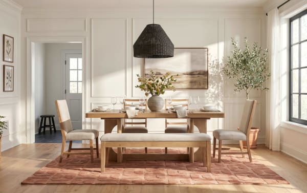 Dining room with natural wood table and bench, beige upholstered chairs, terracotta patterned rug, large window, and black woven pendant light.