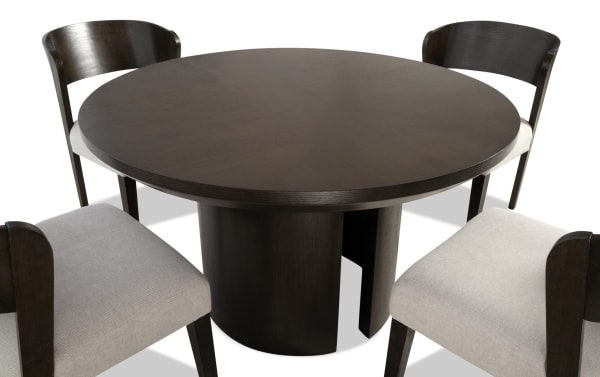 Round dark wood dining table with a cylindrical base, paired with four matching chairs featuring dark wood frames and light beige upholstered seats.