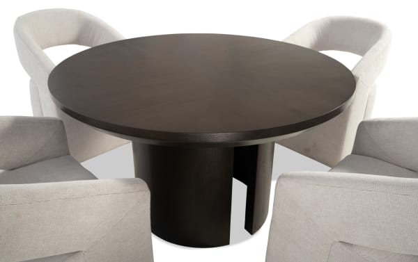 Round dark wood dining table with a solid pedestal base, surrounded by four beige upholstered armchairs with curved backs, modern style.