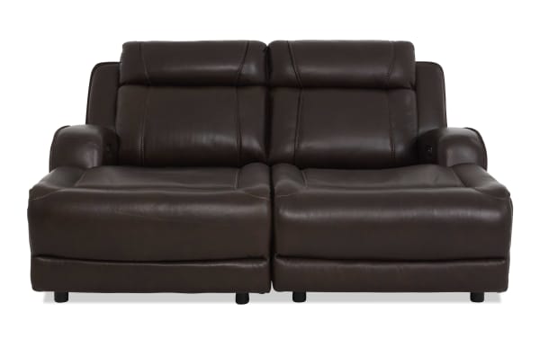 Dark brown leather reclining loveseat with padded armrests and cushioned backrests, featuring visible stitching and a modern design.
