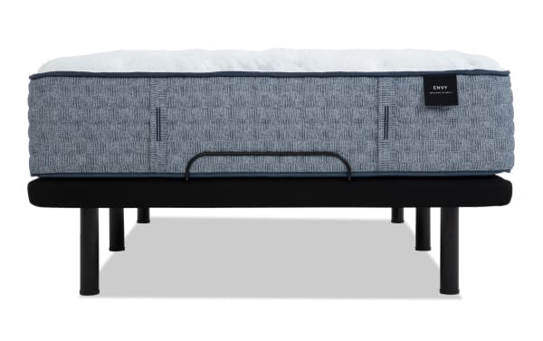 Mattress with gray textured fabric sides and white quilted top on a black metal bed frame. Black label reads "ENVY WELCOME TO BED."