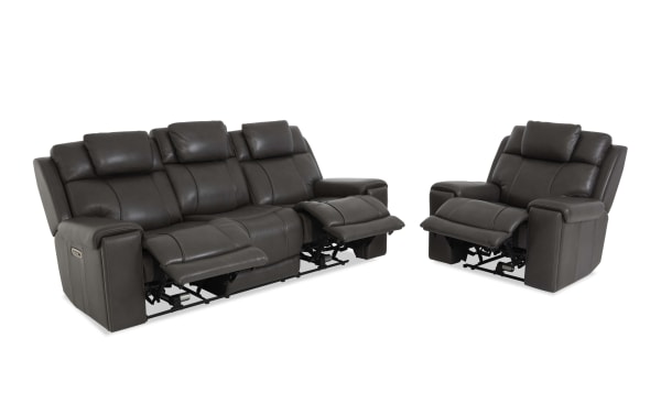 Dark gray leather reclining sofa and armchair set with padded armrests, cushioned backrests, and visible reclining mechanisms, designed for living room comfort.