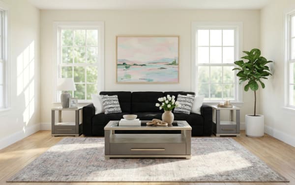 Modern living room with a black fabric sofa, beige wooden coffee table, matching side tables with lamps, a large area rug, and a potted fiddle leaf fig tree.