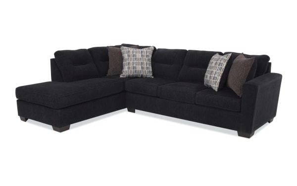 Dark gray fabric sectional sofa with left chaise, tufted back cushions, wooden block legs, and four decorative pillows in patterned and solid brown designs.