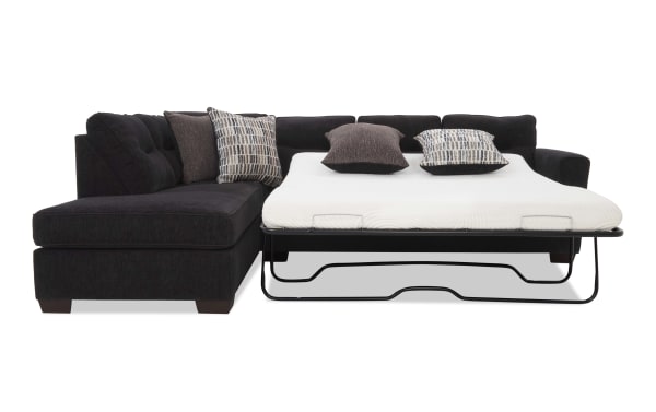 Black fabric sectional sofa with a pull-out bed mattress, featuring tufted cushions and patterned throw pillows, ideal for small living spaces.