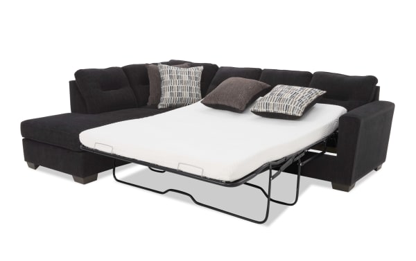 Dark gray fabric sectional sofa with a pull-out metal frame queen-size sleeper mattress and multiple decorative pillows, ideal for space-saving guest accommodation.