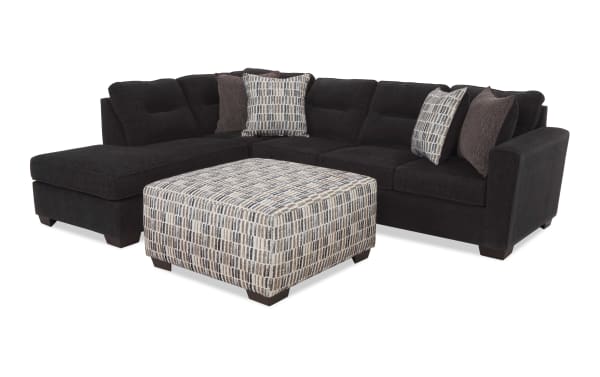 Dark charcoal gray sectional sofa with plush cushions, featuring a matching patterned square ottoman and decorative throw pillows, ideal for modern living rooms.