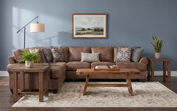 Brown leather sectional sofa with rolled arms, dark wooden legs, and eight decorative patterned throw pillows, ideal for living room seating.